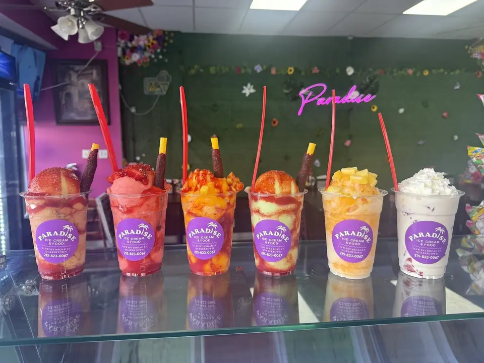 Seis vasos coloridos de postres de fruta con chamoy y palitos de tamarindo en el mostrador de Paradise